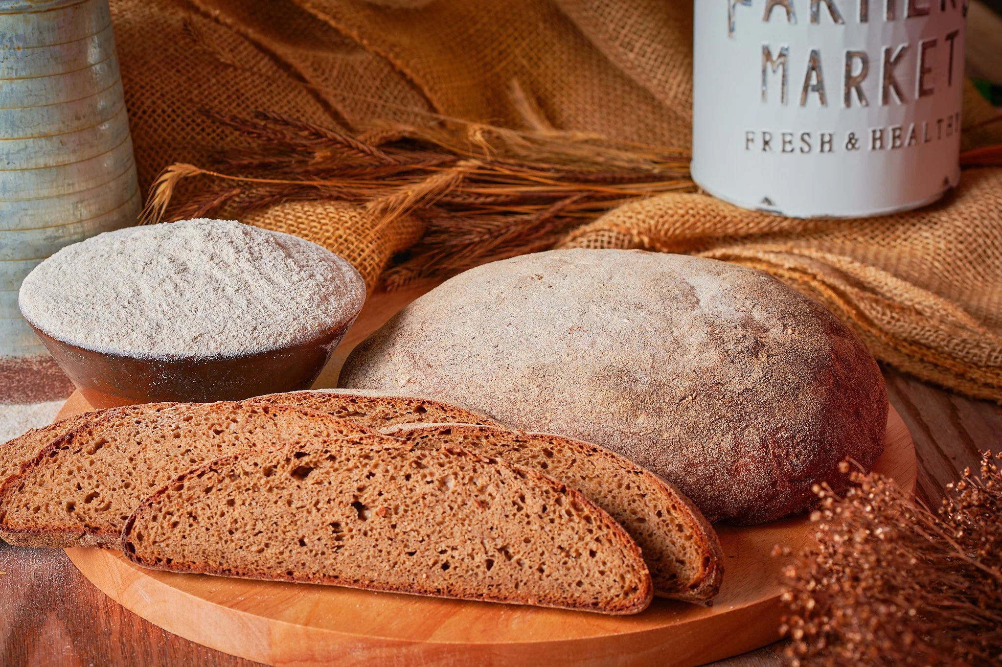 Artfully arranged bread loaf, slices, and a rustic bowl of flour with a vintage flour container prop in a captivating food photography composition.
