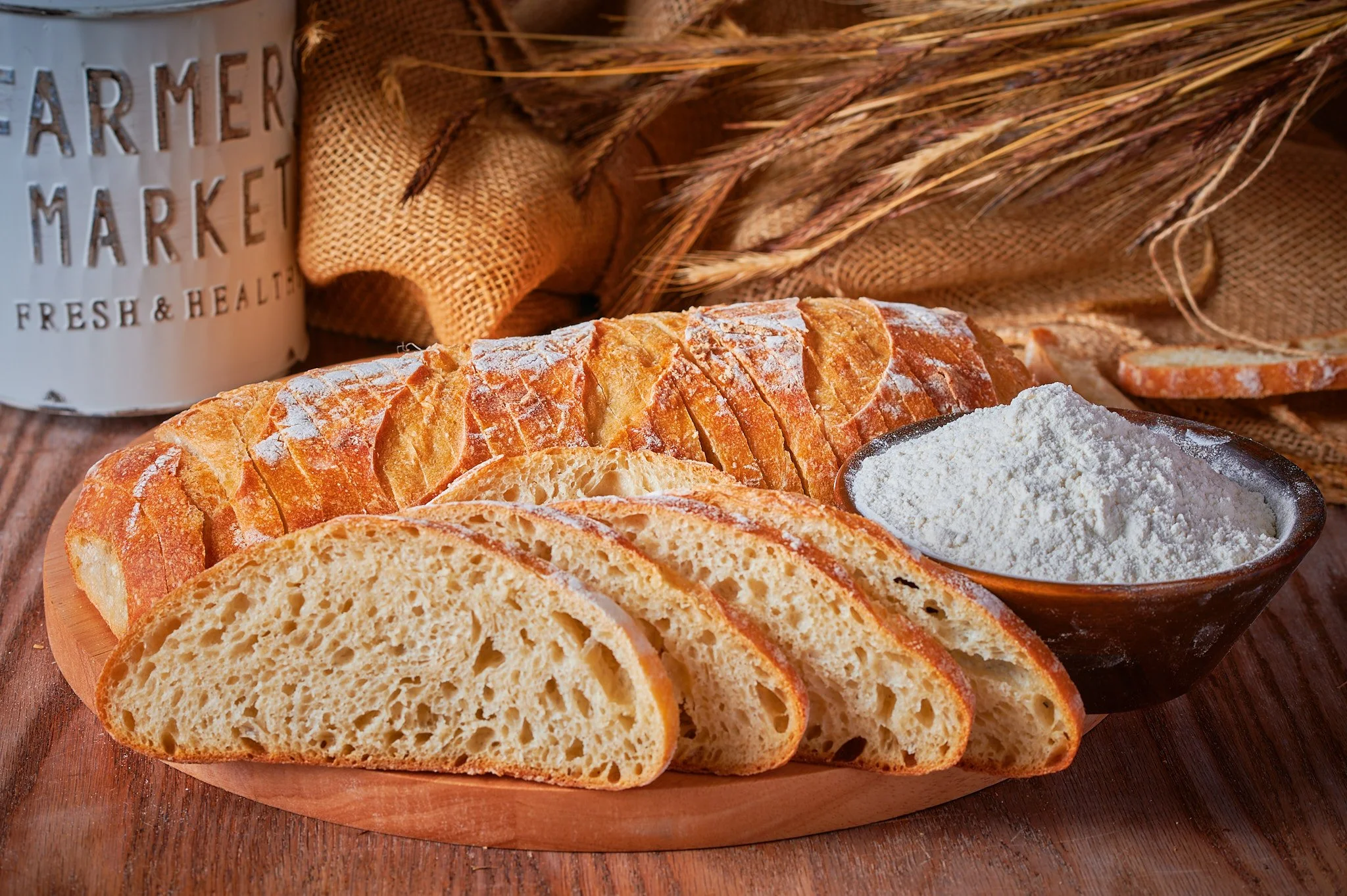 A rustic bread loaf, slices, a bowl of flour, and a flour container, artfully arranged in a food photography composition.