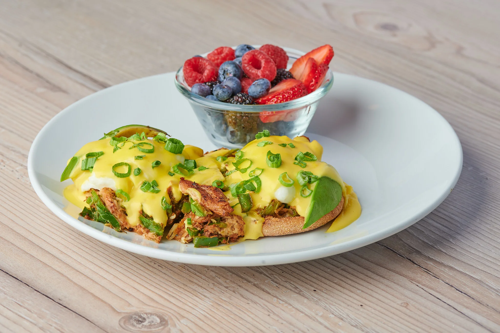Savory Chicken Carnitas Eggs Benedict: A mouthwatering dish featuring two poached eggs, tender chicken carnitas, creamy avocado, spicy jalapeños, all nestled on a toasted English muffin. The dish is elegantly crowned with chives and a zesty ancho hollandaise sauce.