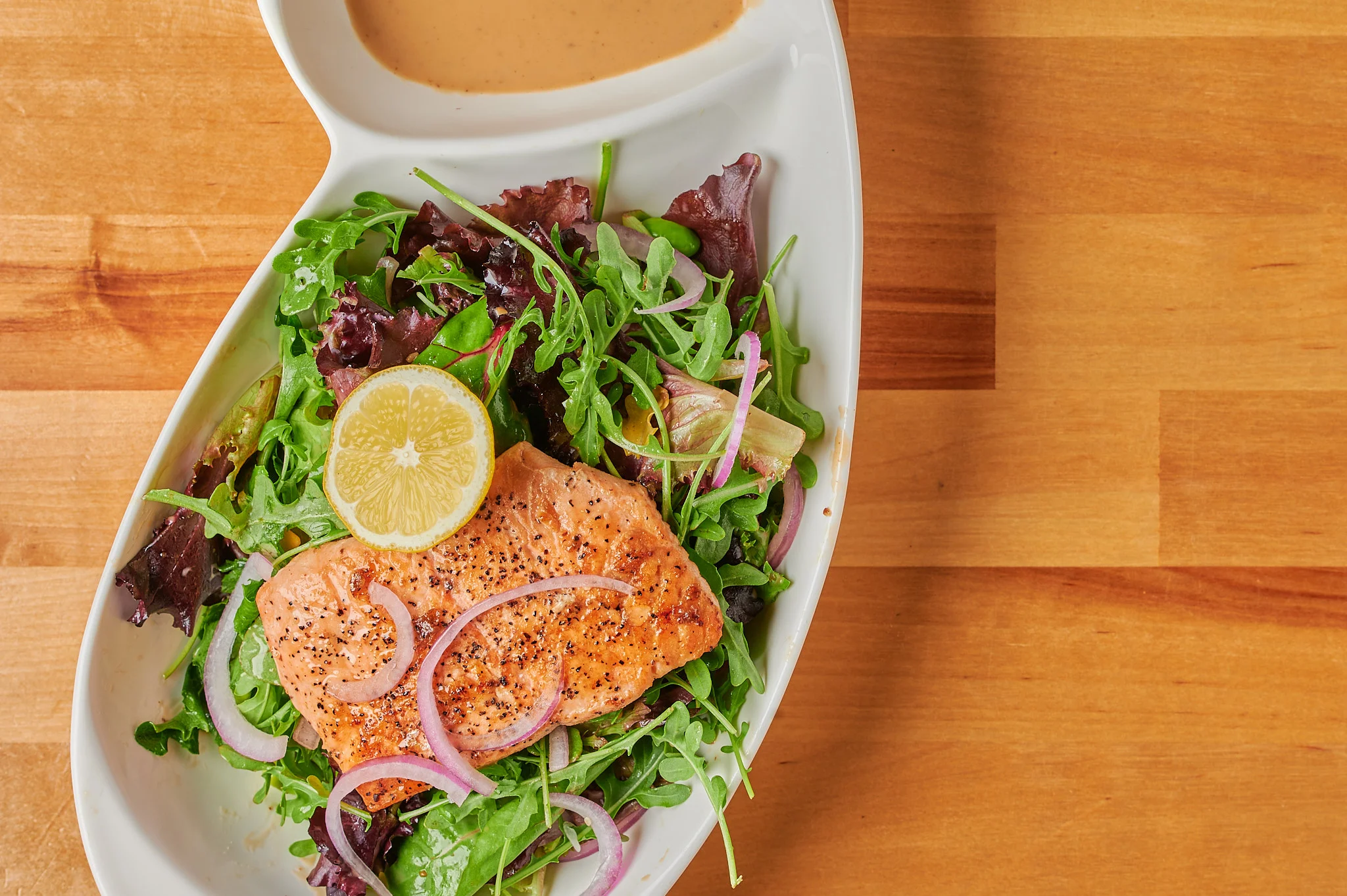 Salmon Salad: A beautifully plated salad featuring fresh, grilled salmon fillet atop a bed of mixed greens, accompanied by colorful cherry tomatoes, cucumber slices, red onion rings, and a drizzle of zesty lemon vinaigrette dressing.