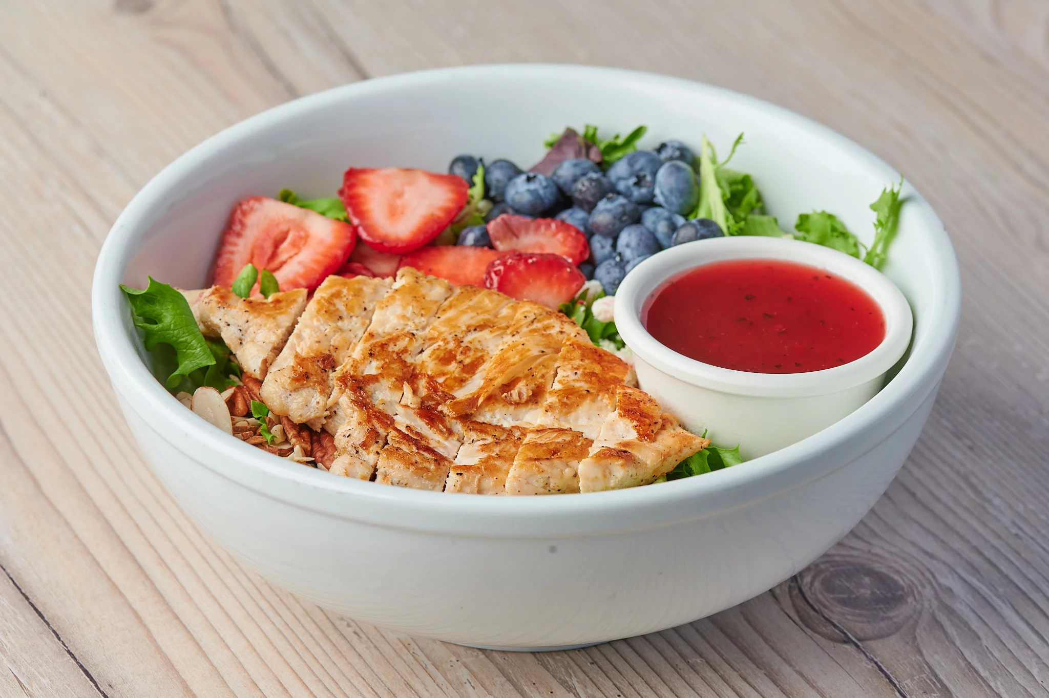 Vibrant Mixed Greens Salad: A colorful mix of fresh greens, ripe strawberries, juicy blueberries, tender grilled chicken breast slices, toasted sliced almonds, crumbled feta cheese, all drizzled with a delightful raspberry vinaigrette dressing.